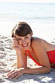 A mature brunette woman on a beach wearing a red bathing suit