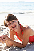 A mature brunette woman on a beach wearing a red bathing suit