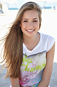 A young blonde woman on a beach wearing a colourful t-shirt