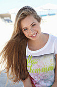 A young blonde woman on a beach wearing a colourful t-shirt