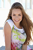 A young blonde woman on a beach wearing a colourful t-shirt