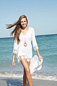 A young blonde woman a white summer hat on a beach wearing a white summer dress