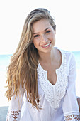 A young blonde woman on a beach wearing a white summer dress