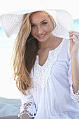 A young blonde woman on a beach wearing a white summer dress and a white summer hat