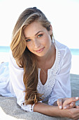 A young blonde woman on a beach wearing a white summer dress