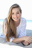 A young blonde woman on a beach wearing a white summer dress