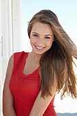 A young blonde woman on a beach wearing a red summer dress