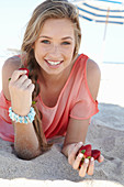 A young blonde woman on a beach wearing a salmon-coloured, off-the-shoulder top