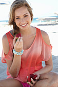 A young blonde woman on a beach wearing a salmon-coloured, off-the-shoulder top