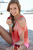 A young blonde woman on a beach wearing a salmon-coloured, off-the-shoulder top