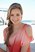 A young blonde woman on a beach wearing a salmon-coloured, off-the-shoulder top