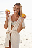 Reife blonde Frau mit Grapefruit in Dessous und Strickjacke am Strand