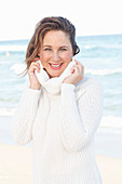 A brunette woman on a beach wearing a white knitted jumper