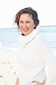 A brunette woman on a beach wearing a white knitted jumper