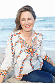 A brunette woman on a beach wearing a printed tunic and jeans