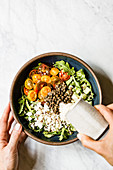 Dressing wird auf Salat mit Quinoa, Linsen, Rucola und Tomaten gegossen