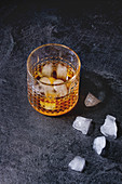 Glass of scotch whiskey on ice standing on black marble table