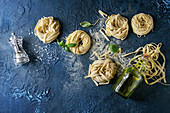 Variety of italian homemade raw uncooked pasta spaghetti and tagliatelle with basil leaves, olive oil, salt, pepper, semolina flour