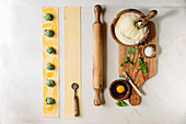 Ingredients for homemade italian pasta ravioli staffed by spinach ricotta, semolina flour, egg yolk, basil, olive wood utensils bowls, scoop and rolling pin