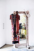 Standing mirror with wooden frame, caftan and hat hung over the mirror