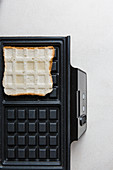 A slice of bread being toasted in a waffle iron