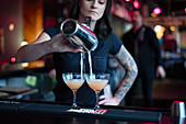 Barkeeperin gießt Cocktails aus Shaker in Gläser