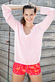 A brunette woman wearing a pink jumper and shorts