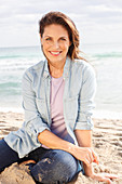 Brunette woman wearing denim blouse and jeans on beach