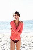 Reife, brünette Frau in schwarzem Bikini und rotem Shirt am Strand