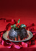 English Christmas pudding with flames and holly garnish on pewter plate