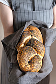 Girl in an apron holding a challah with poppy seeds on a linen napkin