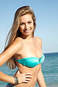 A young blonde woman on a beach wearing a turquoise bikini