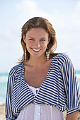 A young brunette woman on a beach wearing a black-and-white striped top