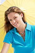 Junge brünette Frau im blauen Shirt vor gelbem Sonnenschirm