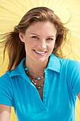 A young brunette woman wearing a blue shirt in front of a yellow parasol