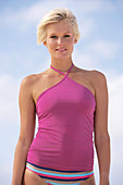 A mature blonde woman with short hair on a beach wearing a purple top