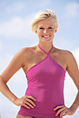 A mature blonde woman with short hair on a beach wearing a purple top