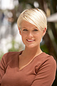 A mature blonde woman with short hair outside wearing a brown top