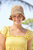 A mature blonde woman with short hair outside wearing a yellow top and a hat