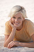 A mature blonde woman with short hair on a beach wearing a striped bikini and an orange top