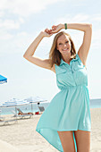 A young blonde woman on a beach wearing a light-blue summer dress