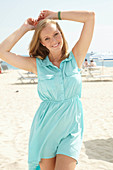 A young blonde woman on a beach wearing a light-blue summer dress