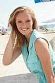 A young blonde woman on a beach wearing a light-blue summer dress