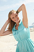 A young blonde woman on a beach wearing a light-blue summer dress