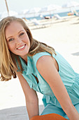 A young blonde woman on a beach wearing a light-blue summer dress