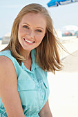 A young blonde woman on a beach wearing a light-blue summer dress