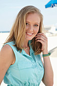 A young blonde woman on a beach wearing a light-blue summer dress