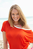 A young blonde woman on a beach wearing a purple bikini and an orange top