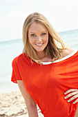 A young blonde woman on a beach wearing a purple bikini and an orange top