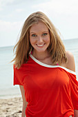 A young blonde woman on a beach wearing a purple bikini and an orange top